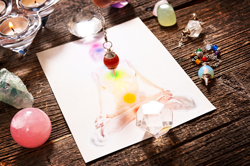 Chakras illustrated over human body with natural crystals and pendulum